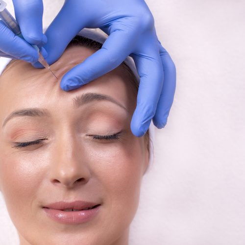 Doctor with rubber gloves doing a plastic face surgery on a happy young female Botox Anti-wrinkle Treatment